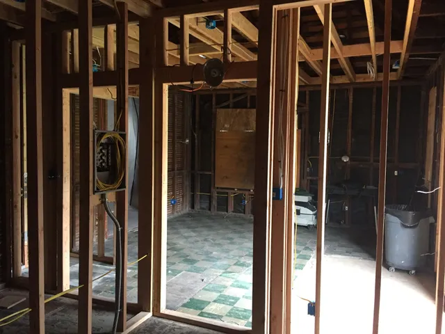 Unfinished interior with exposed wooden framing, wiring, and a checkered floor in a dim room.