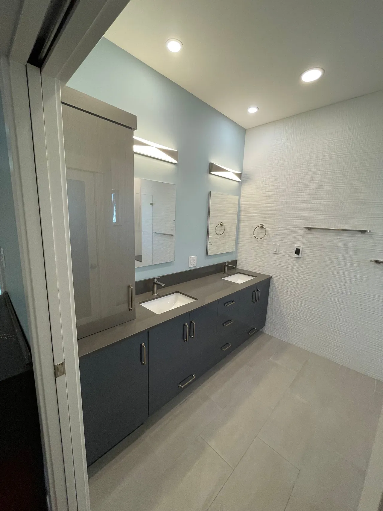 Modern bathroom with double vanity, large mirror, gray cabinets, white walls, and recessed lighting