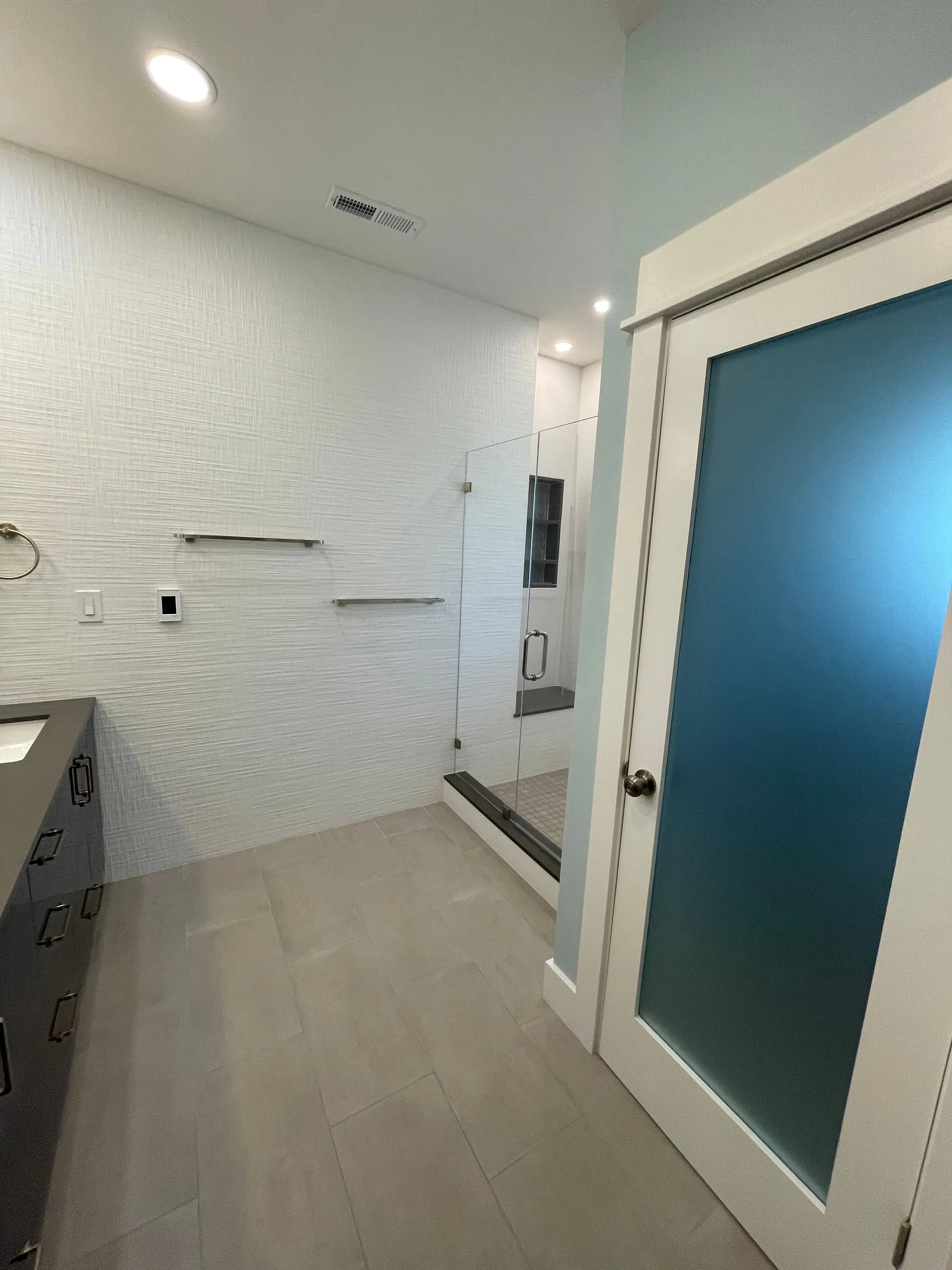 Bright modern bathroom with white walls, gray floor, vanity, and frosted glass shower door