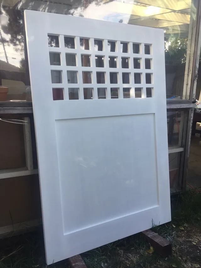 White paneled door with a grid of small square windows at the top, leaning outdoors.