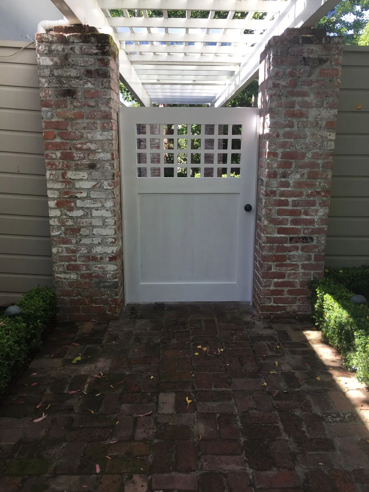 White gate between brick pillars in a shaded brick courtyard under a pergola