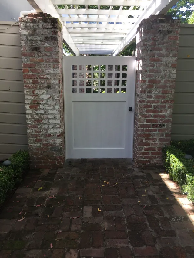 White gate between brick pillars in a shaded brick courtyard under a pergola
