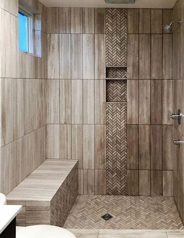 A bathroom with a walk in shower with a bench and a window.
