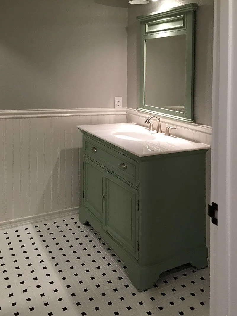 A bathroom with a green vanity and a mirror.