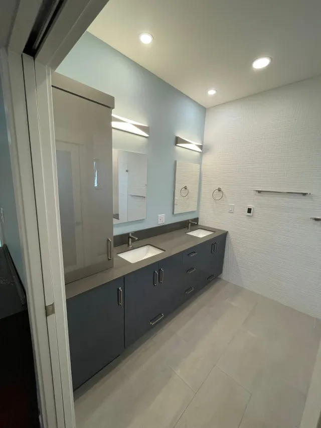 Modern bathroom with dark vanity, double mirrors, white textured walls, and bright ceiling lights