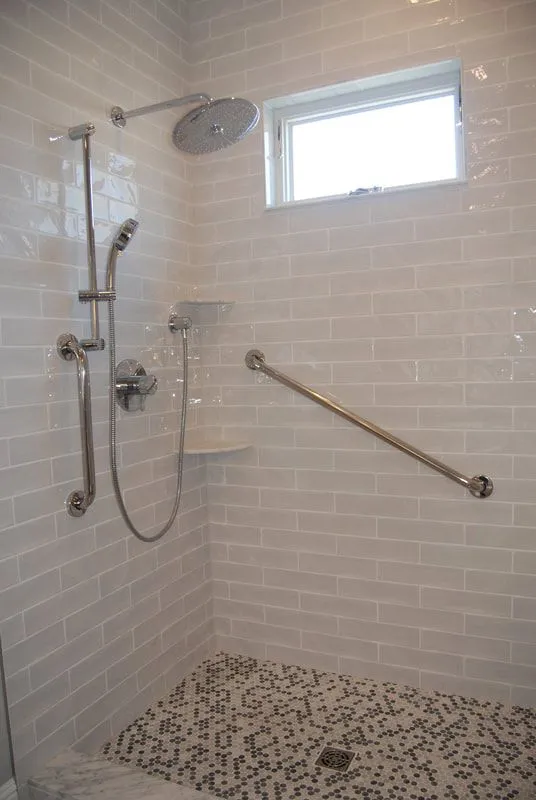 A walk in shower with a stainless steel handle and a window.