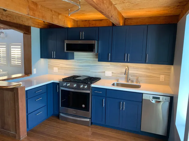 A kitchen featuring blue cabinets, stainless steel appliances, white countertops, and a wood-beamed ceiling.